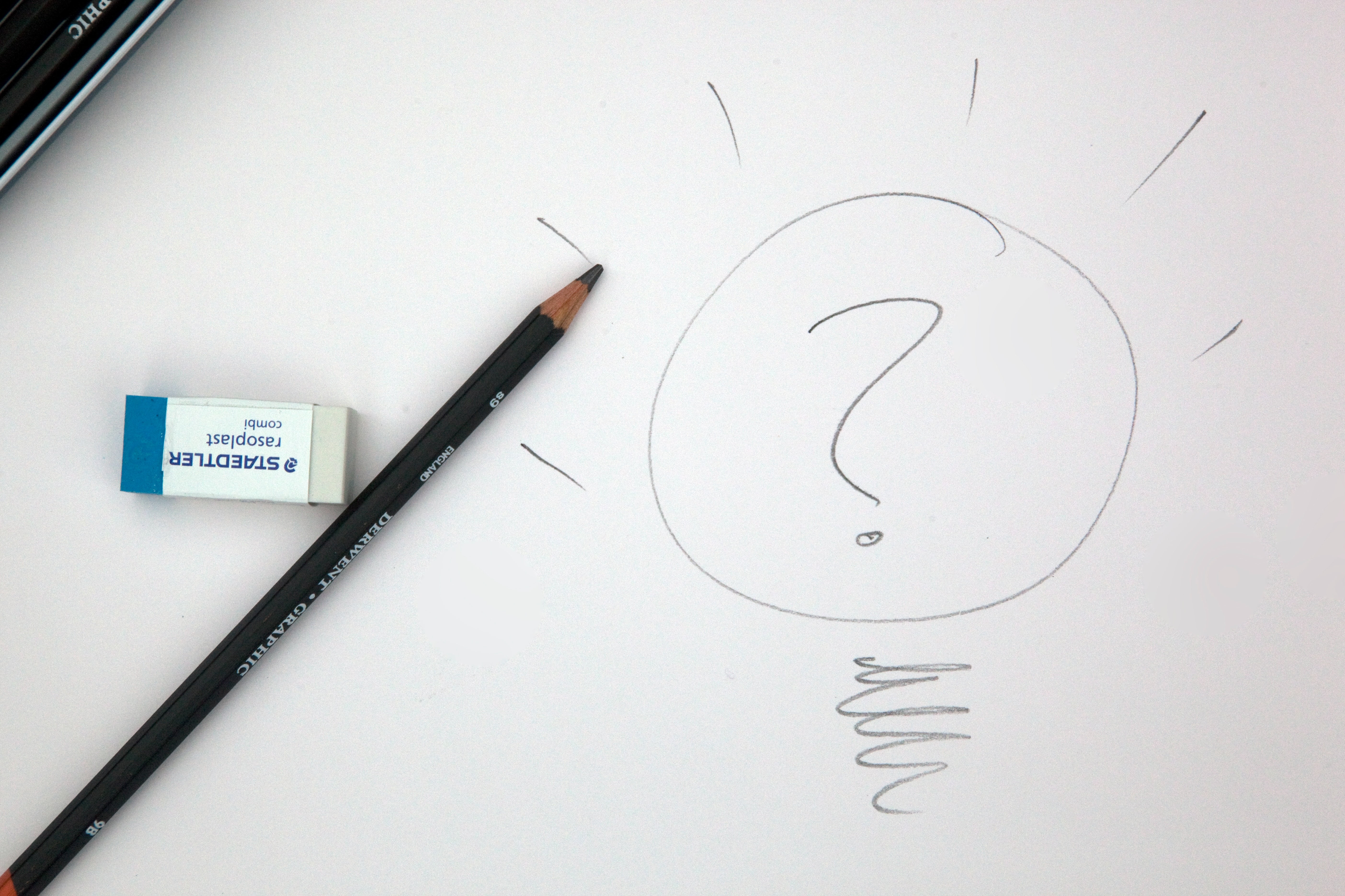 A black pencil and Staedtler Eraser on top of a pencil drawing of a question mark inside of a lightbulb
